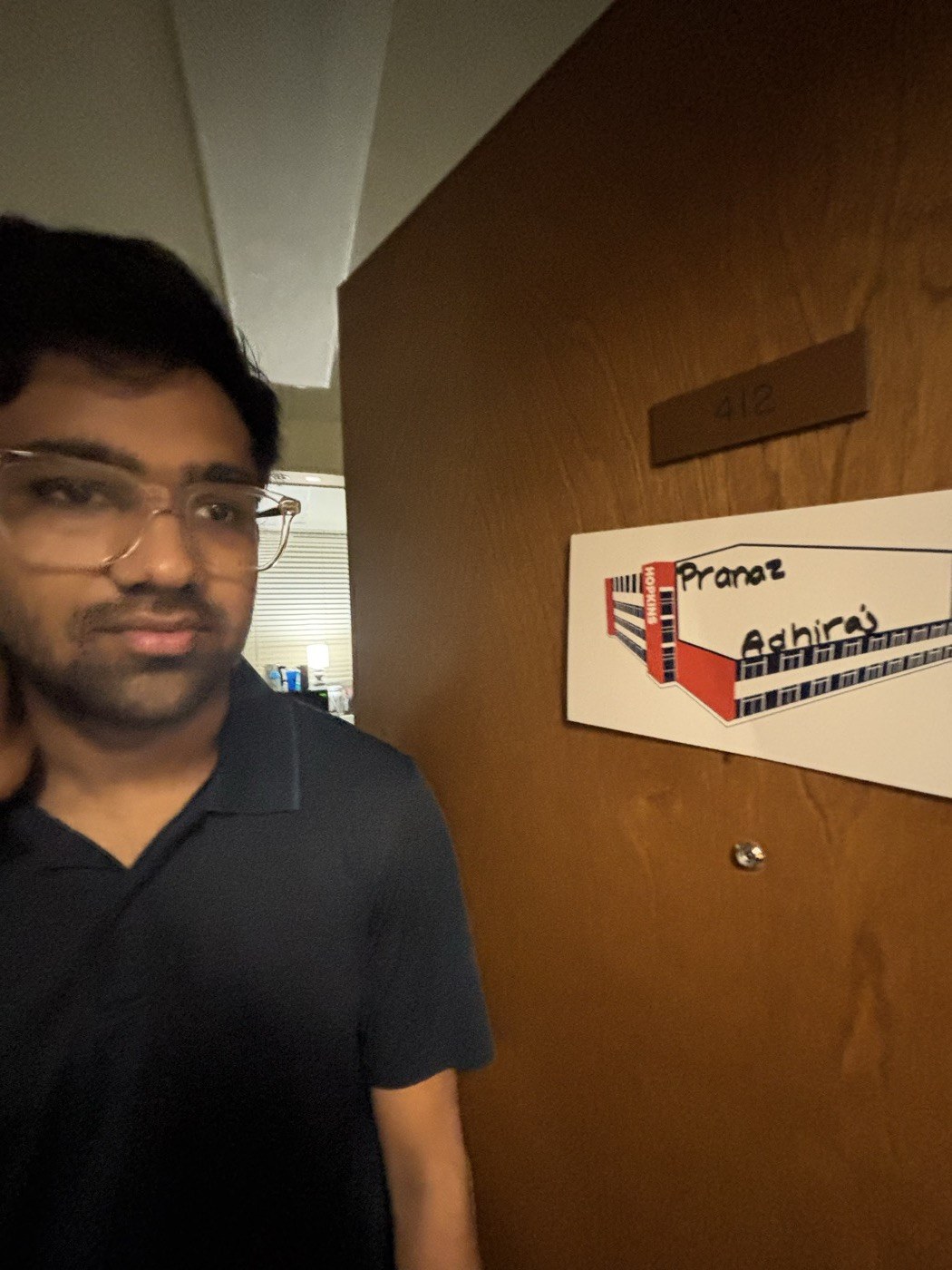 Pranav posing next to his dorm door nameplate
