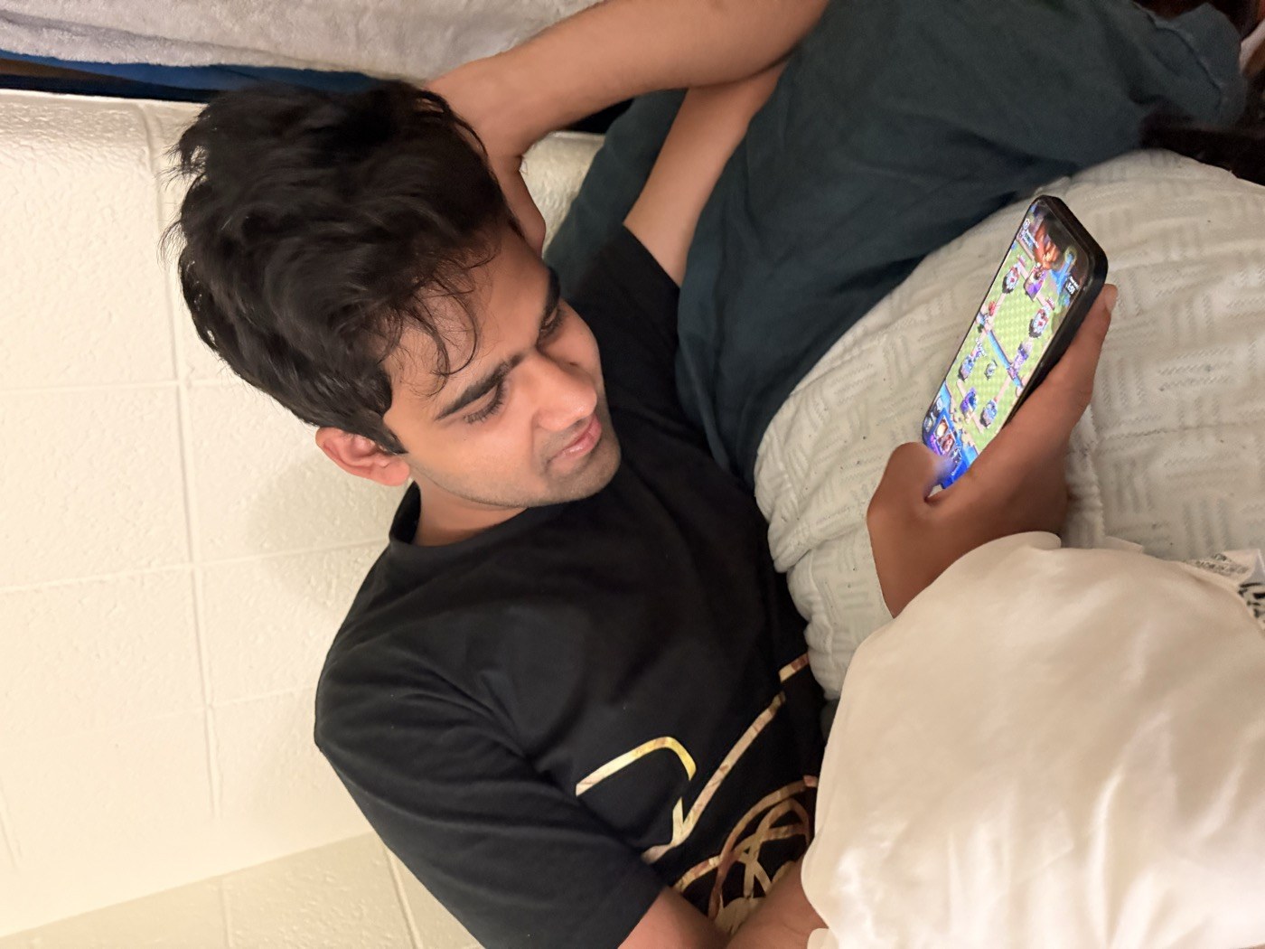 Pranav lying in bed playing a mobile game